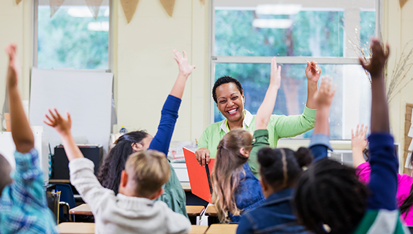 teacher in a classroom raising her hand with students
