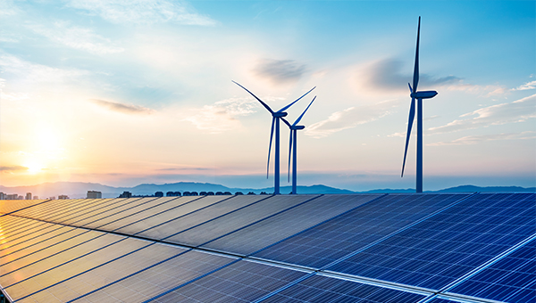 Solar panels with wind turbines in the background and the sun setting