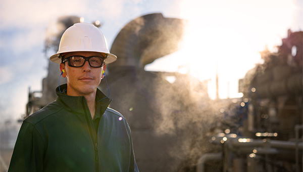 Employee in a white hardhat in front of an industrial plant