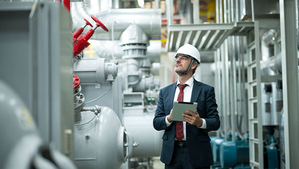 Professional wearing a hard hat uses a tablet while inspecting industrial equipment in a manufacturing facility