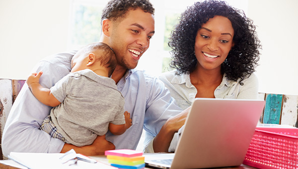 Family smiling while holding their baby and looking at a laptop