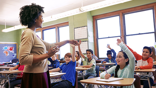 An elementary school teacher teaching students as the students raise their hands