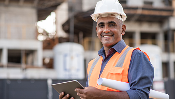 Contractor with white hard hat holding a tablet and blueprints