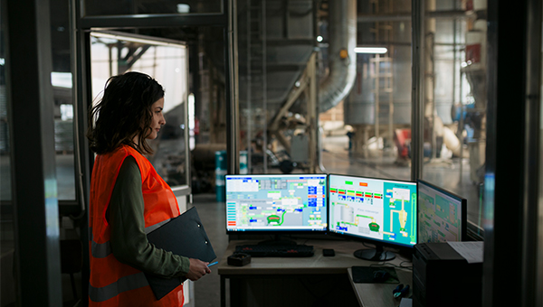 Employee in an orange safety vest at a warehouse looking at computer monitors