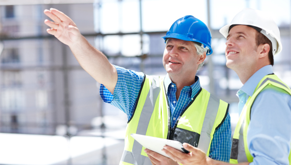 Two contractors standing outside with hard hats and safety vets