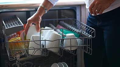 Woman loading white dishes on to the dish washer.