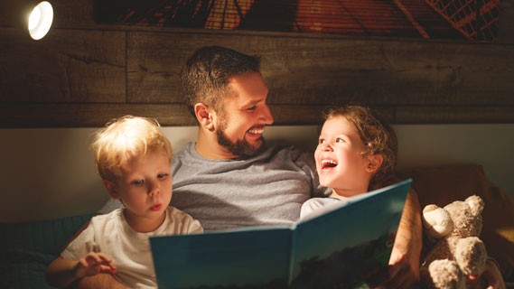 Dad reading a bed time story to children under the lamp light.